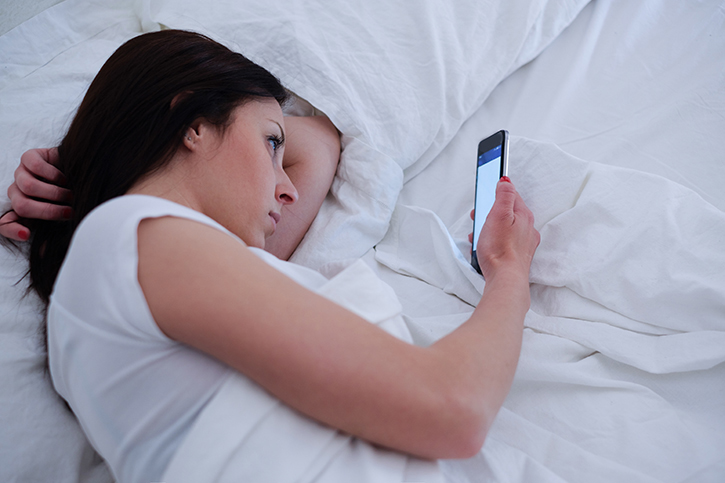 Young woman using phone lying in bed