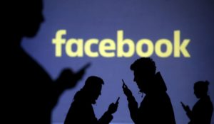 FILE PHOTO: Silhouettes of mobile users are seen next to a screen projection of Facebook logo in this picture illustration