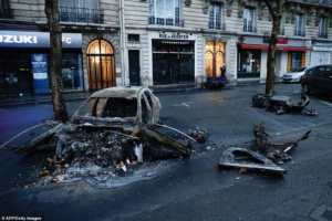 The burned-out shell of a car lies in the street