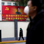 People wearing masks walk past a portrait of Chinese President Xi Jinping on a street as the country is hit by an outbreak of coronavirus in China