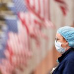 masked, gowned nurse, US flags behind