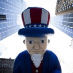 cartoon- sad Uncle Sam in row of office bldgs