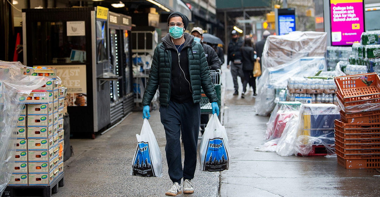 Masked person with gloves carries 2 plastic shopping bags