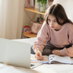 Girl doing school on her laptop on a bed