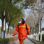 City Worker sprays trees in Park wearing mask