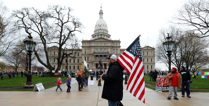 man with flag in front of Lansing, MI capital