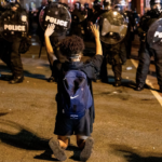 Protestor kneels before line of police