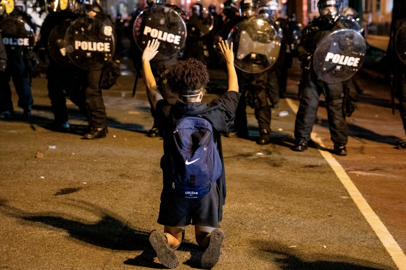 Protestor kneels before line of police