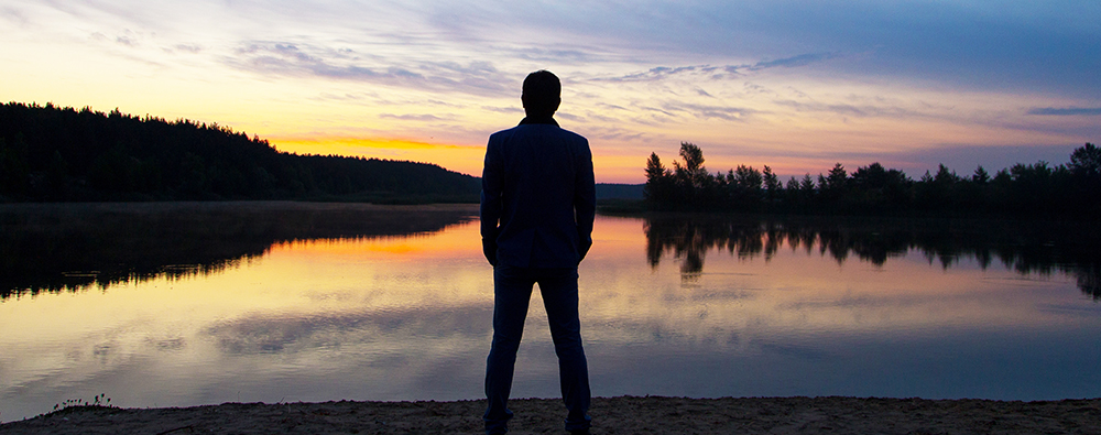 A man in a suit watches the sunset on the lake shore