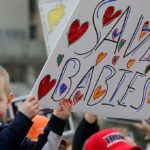 Small child holds Save-The-Babies sign