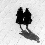 2 graduates walk across paved plaza