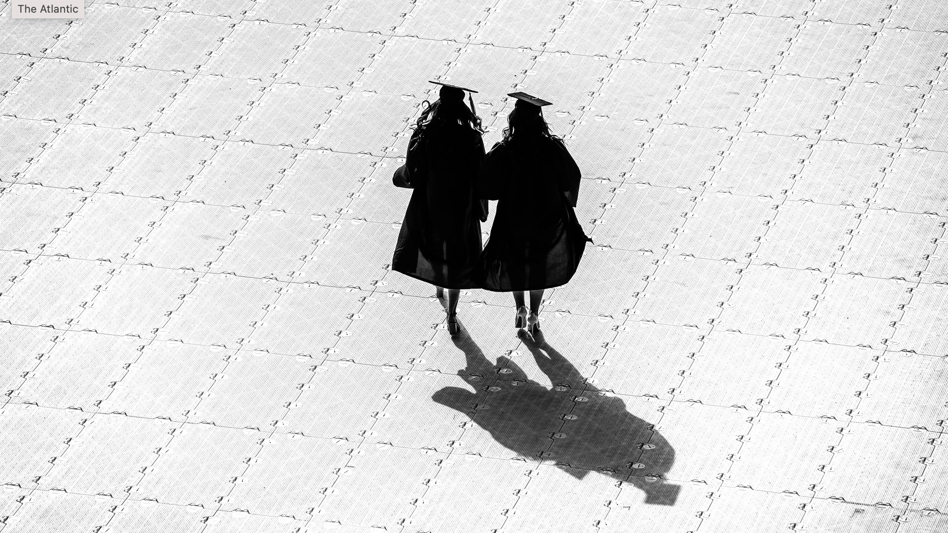 2 graduates walk across paved plaza