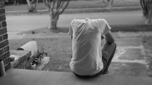 young man sits slumped on front stoop