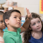 small children in classroom raising hands