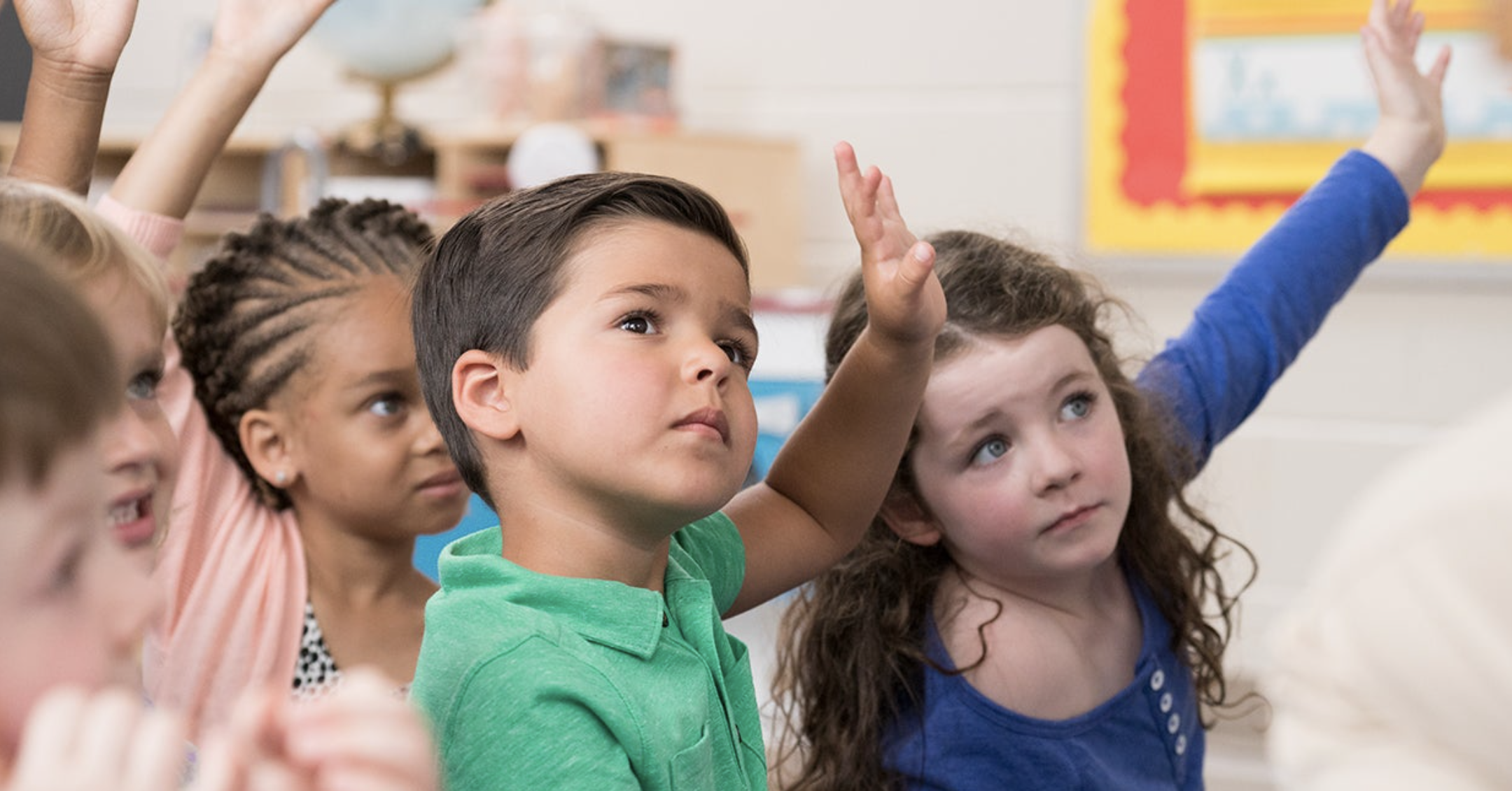 small children in classroom raising hands