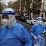 Men in protective suits walk in the street as outbreaks of coronavirus continue in Beijing, China