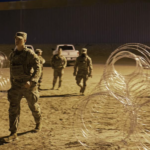 Soldiers walk between rolls of concertina wire - sepia