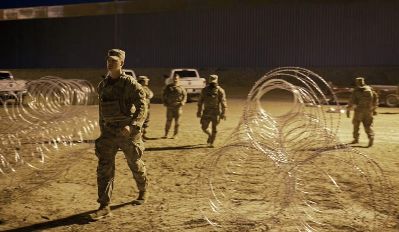 Soldiers walk between rolls of concertina wire - sepia