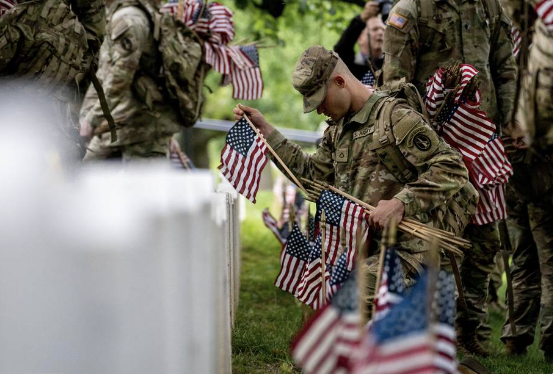 soldiers in fatigues place flags on graves