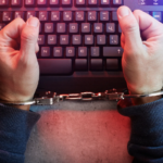 man handcuffed at computer keyboard