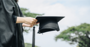 Graduate in gown holds motarboard cap