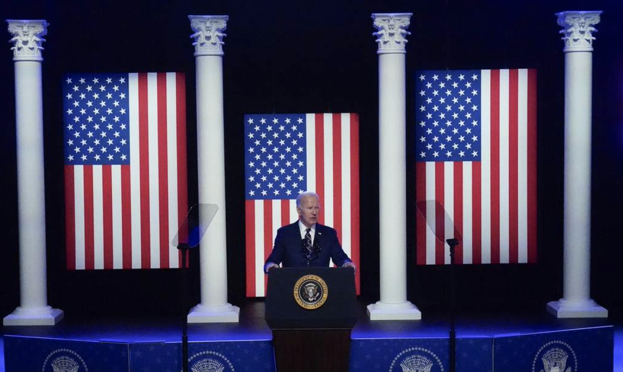 Biden at presidential podium with 3 giant US flags