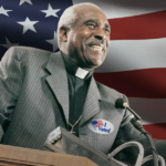 Pastor at pulpit has I voted sticker in front of giant US flag