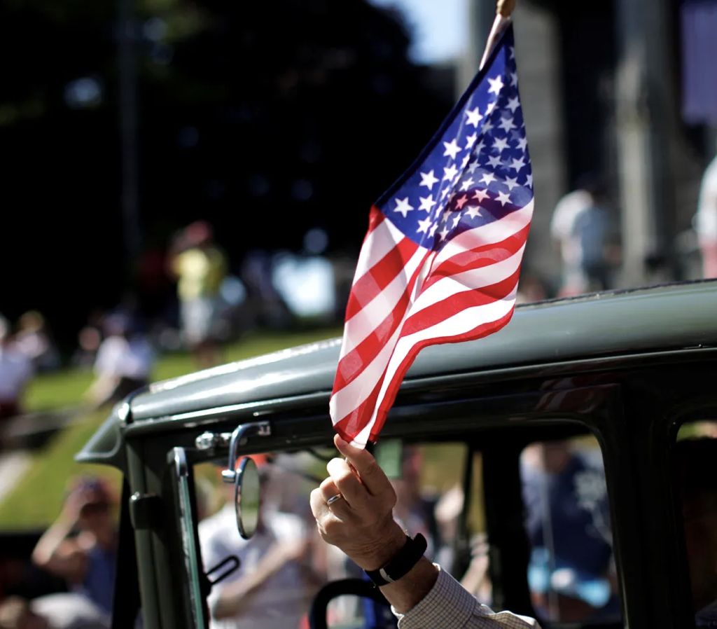 man waves US Flag from car window during parade