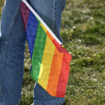 blue jean person holds rainbow gay flag