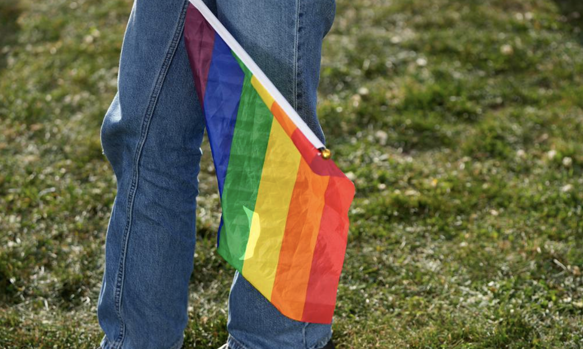 blue jean person holds rainbow gay flag