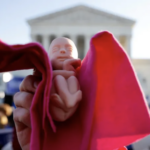 pro-life activist holds a baby doll during a protest outside the Supreme Court building