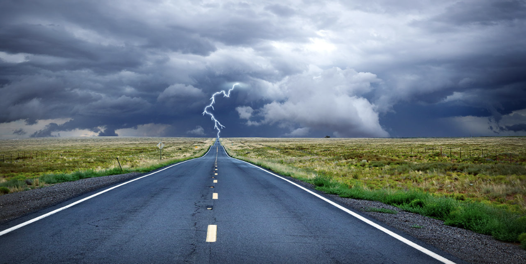 long straight 2-lane road heading into storm Lightening