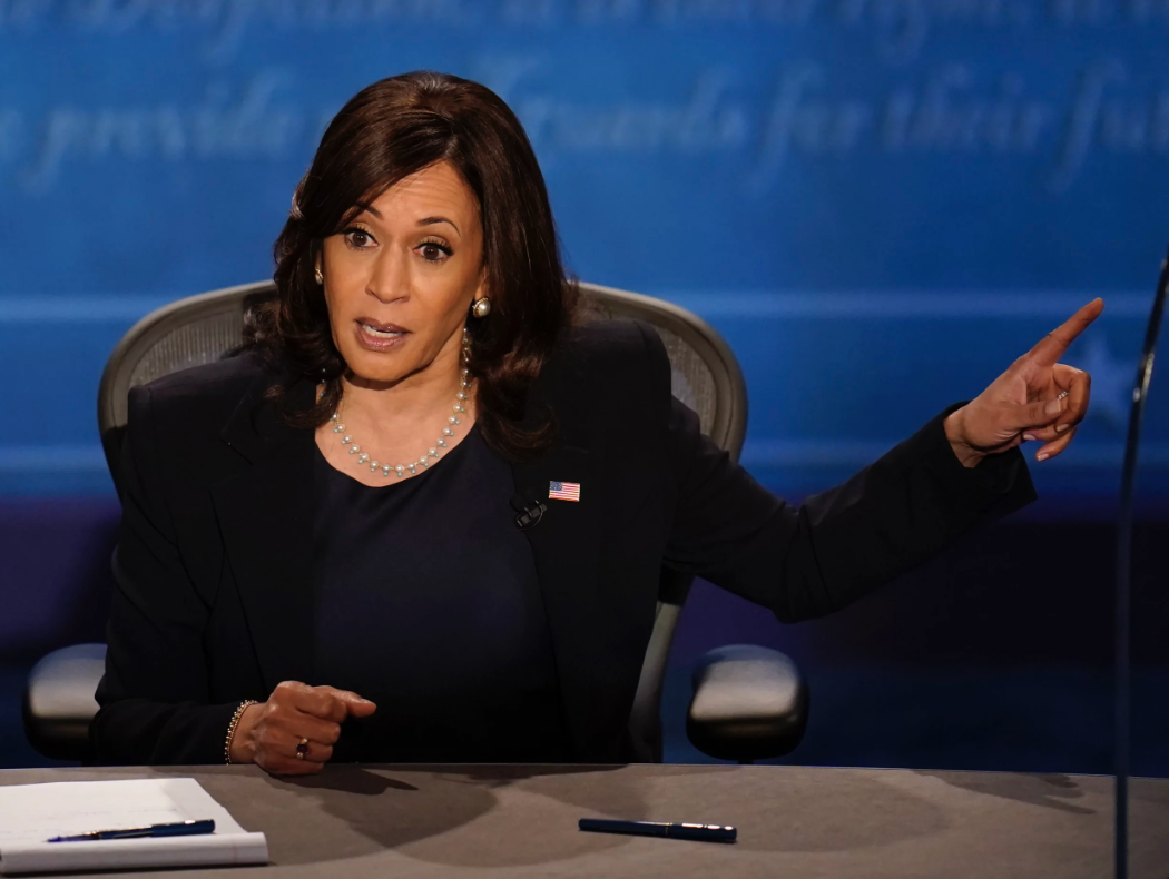 Kamala at table speaks and points