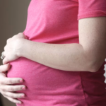 Pregnant woman in pink holds tummy