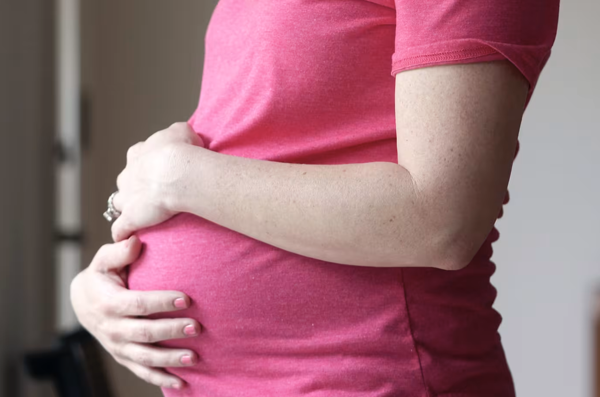 Pregnant woman in pink holds tummy