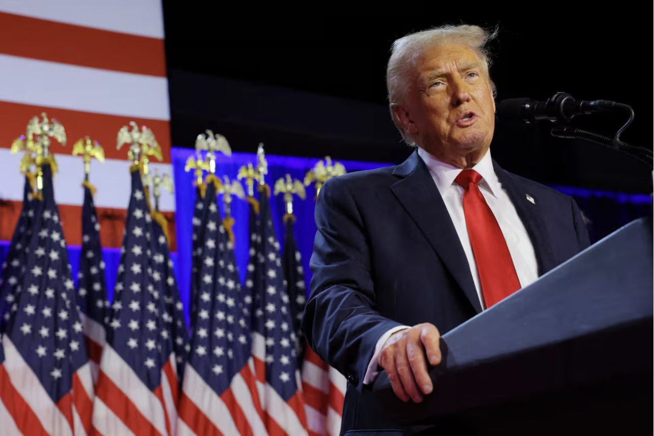 Donald Trump at lecturn in front of row of US Flags