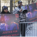 2 protesters behind barricade with Justice for Jordan Neely signs