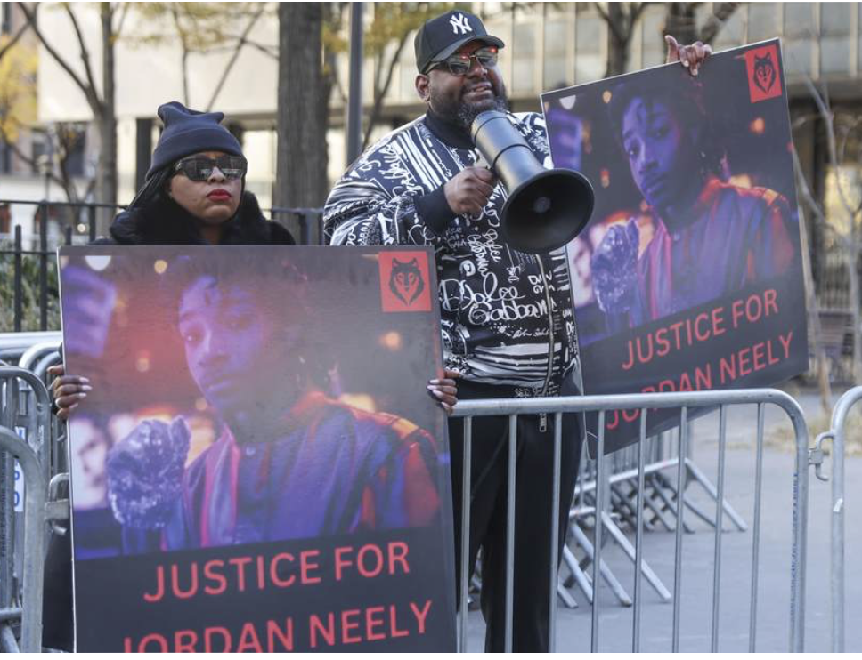 2 protesters behind barricade with Justice for Jordan Neely signs