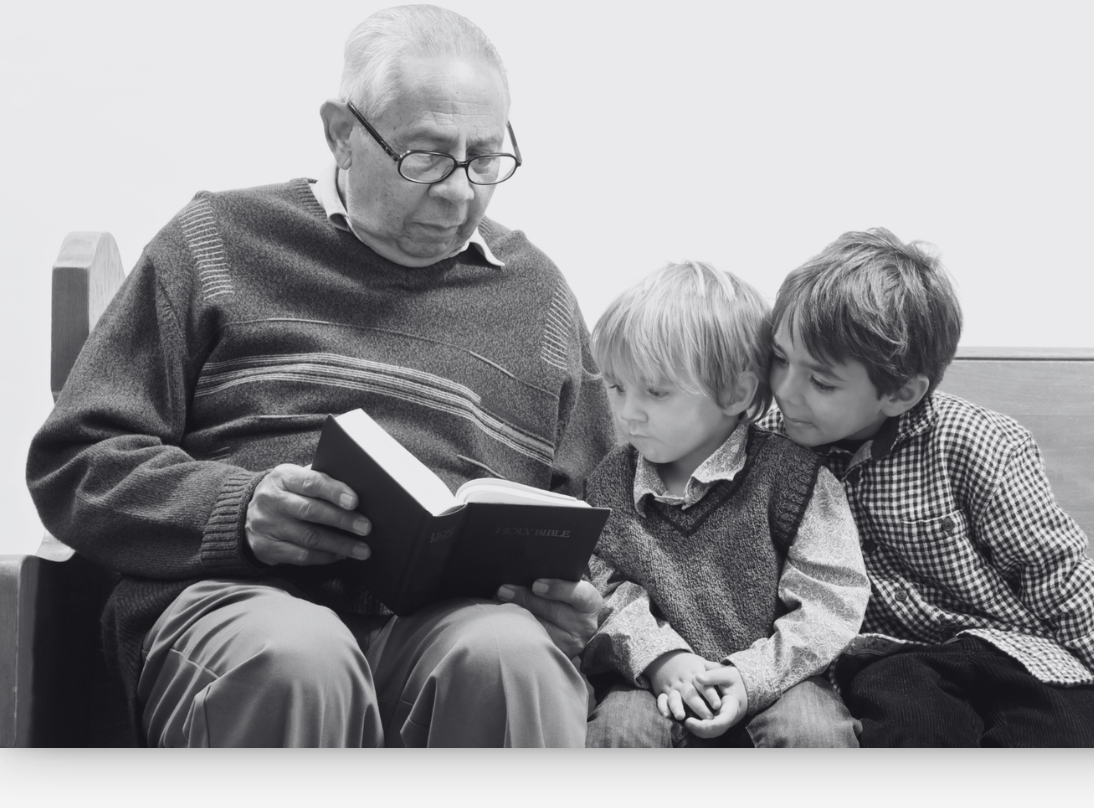 bandw - older man reads Bible to children on church pew