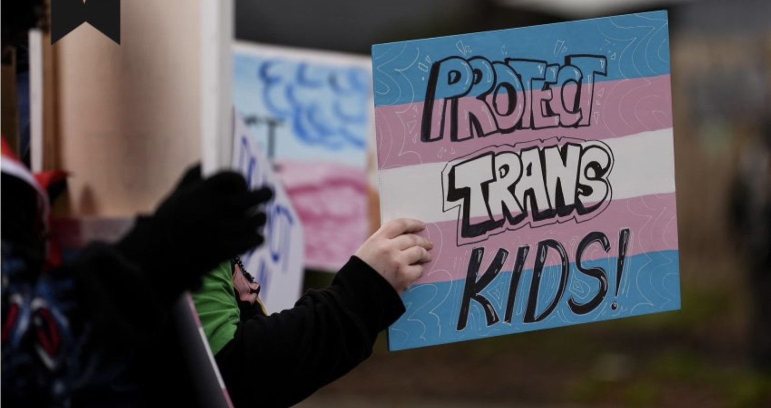 Protect Trans Kids sign - held by hands in the dark