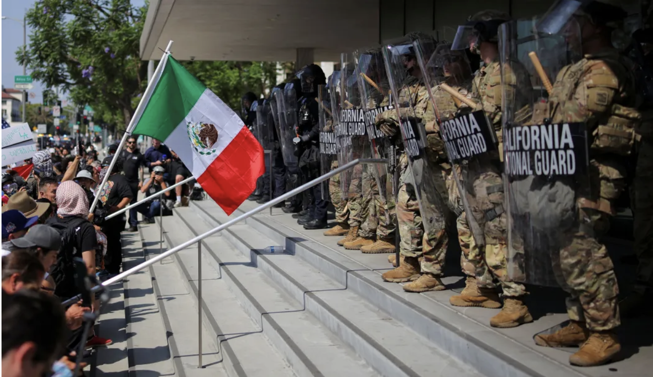demonstrator waves a Mexican flag in front of California National Guard troops in LA